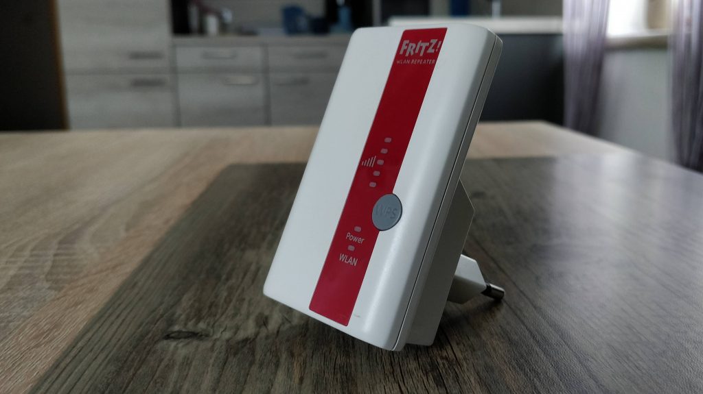 Der FRITZ!Repeater 310 steht auf einem Holztisch, im Hintergrund sieht man verschwommen eine moderne Küche